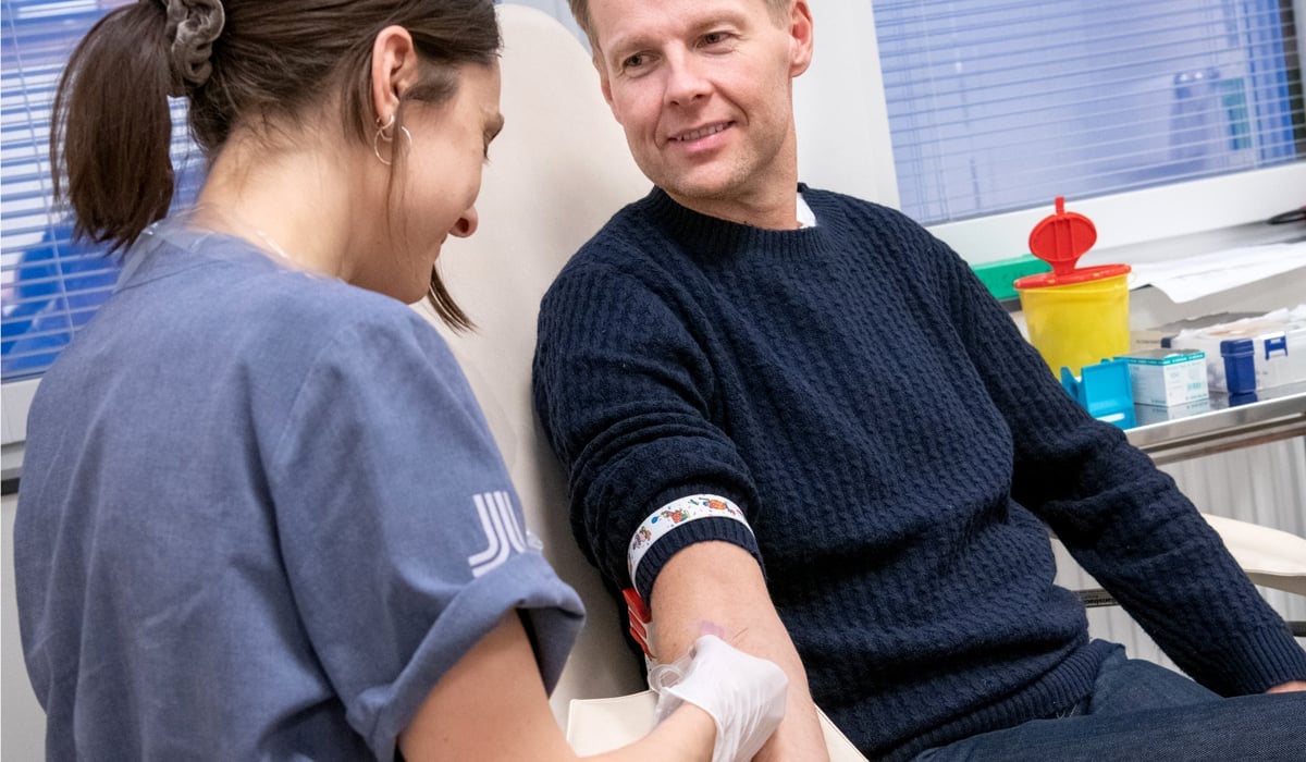 Bild på en kvinna i sjukhuskläder som tar ett blodprov på en man som sitter i en sjukhusstol