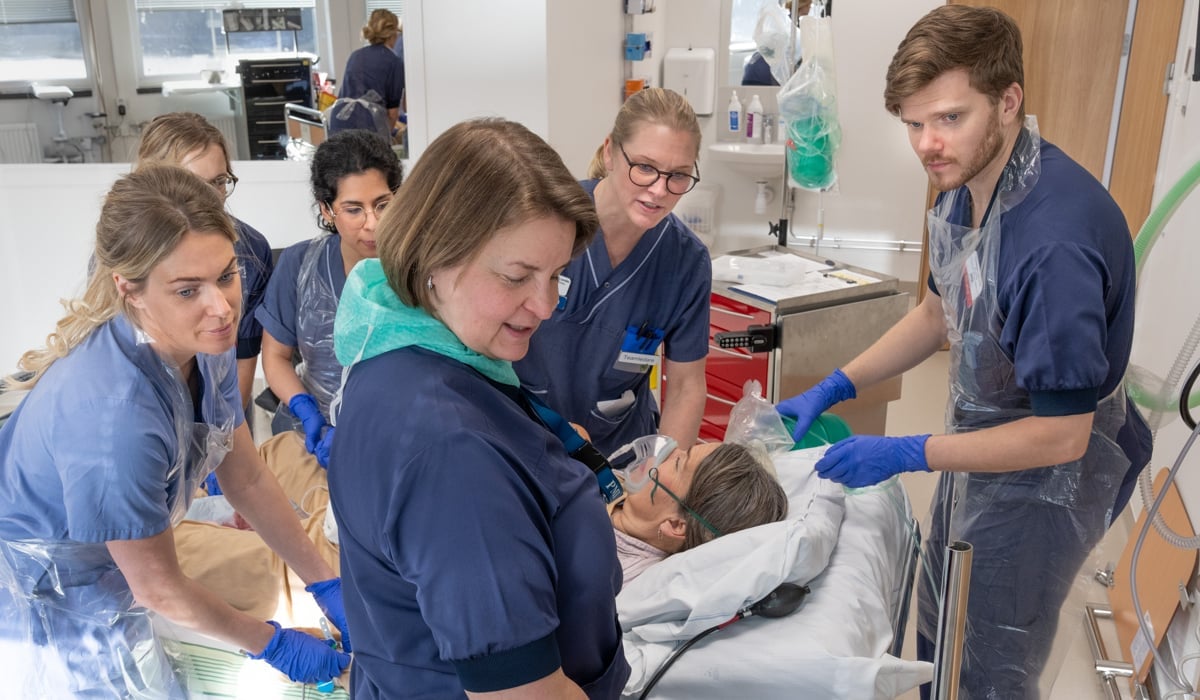 6 personer som utför en övning 5 kvinnor och en man. 1 person som ligger i sjukhussäng och agerar patient.