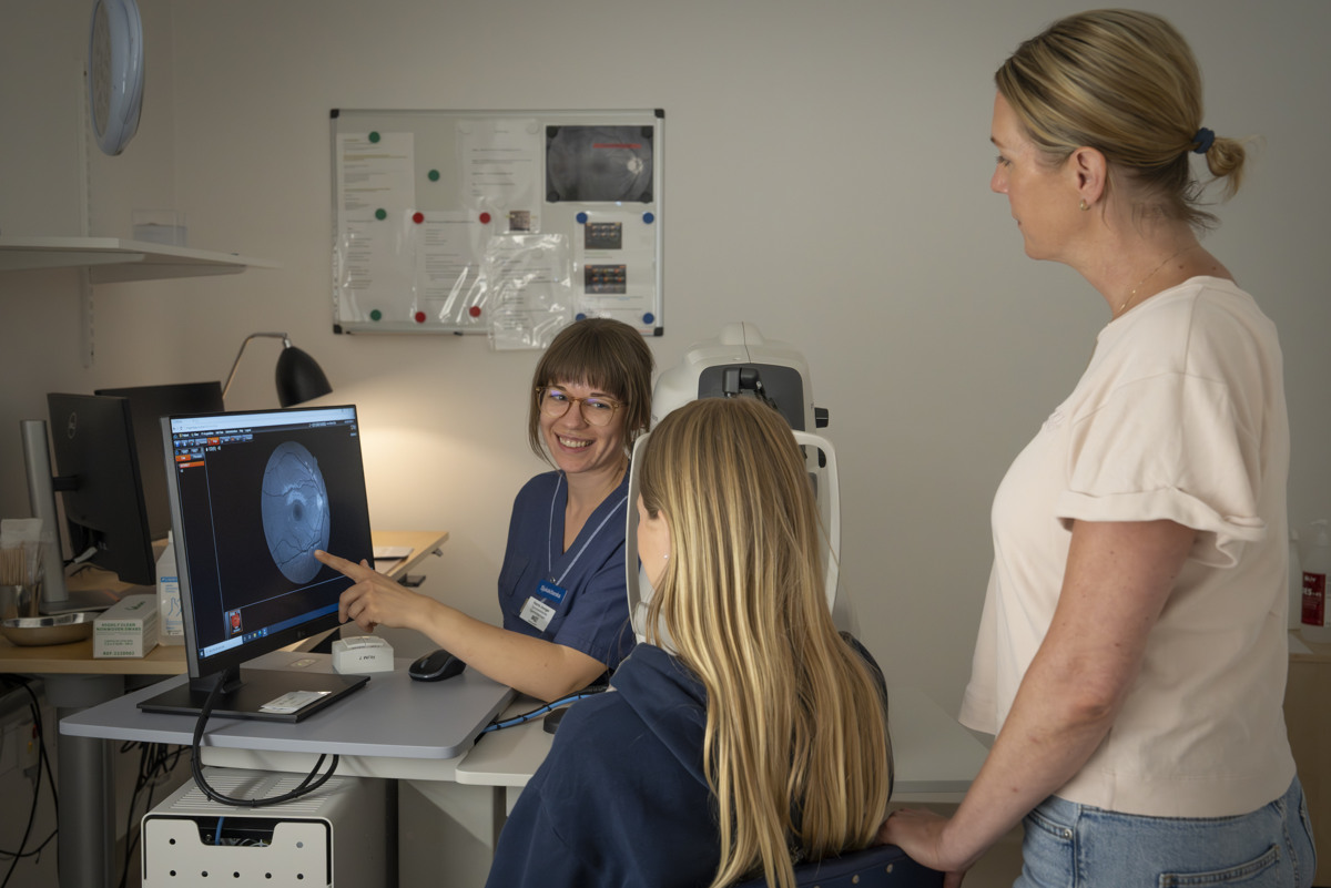 En sjuksk&ouml;terska som pekar p&aring; en sk&auml;rm med en bild p&aring; ett &ouml;ga. Bredvid sjuksk&ouml;terskan sitter en ung kvinna och kollar p&aring; sk&auml;rmen med en annan kvinna som st&aring;r bakom henne. 