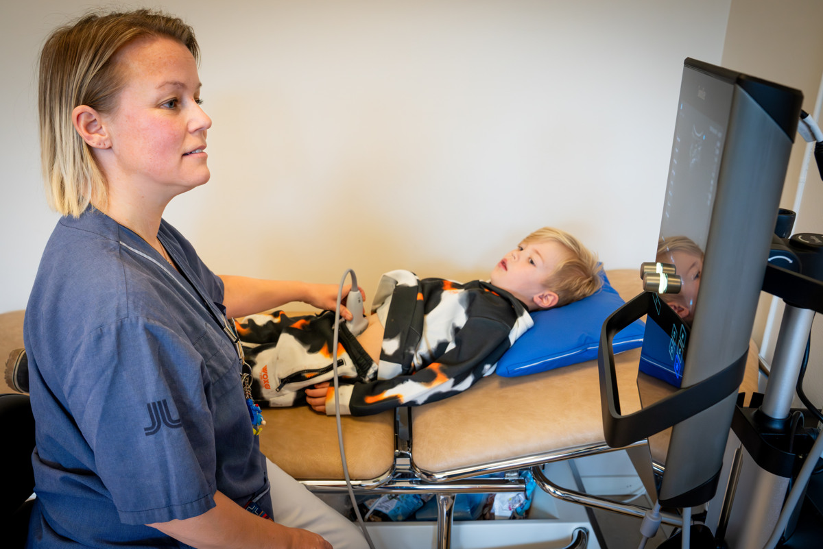 En kvinnlig sjuksk&ouml;terska som h&aring;ller en ultraljudsmaskin mot ett barns mage