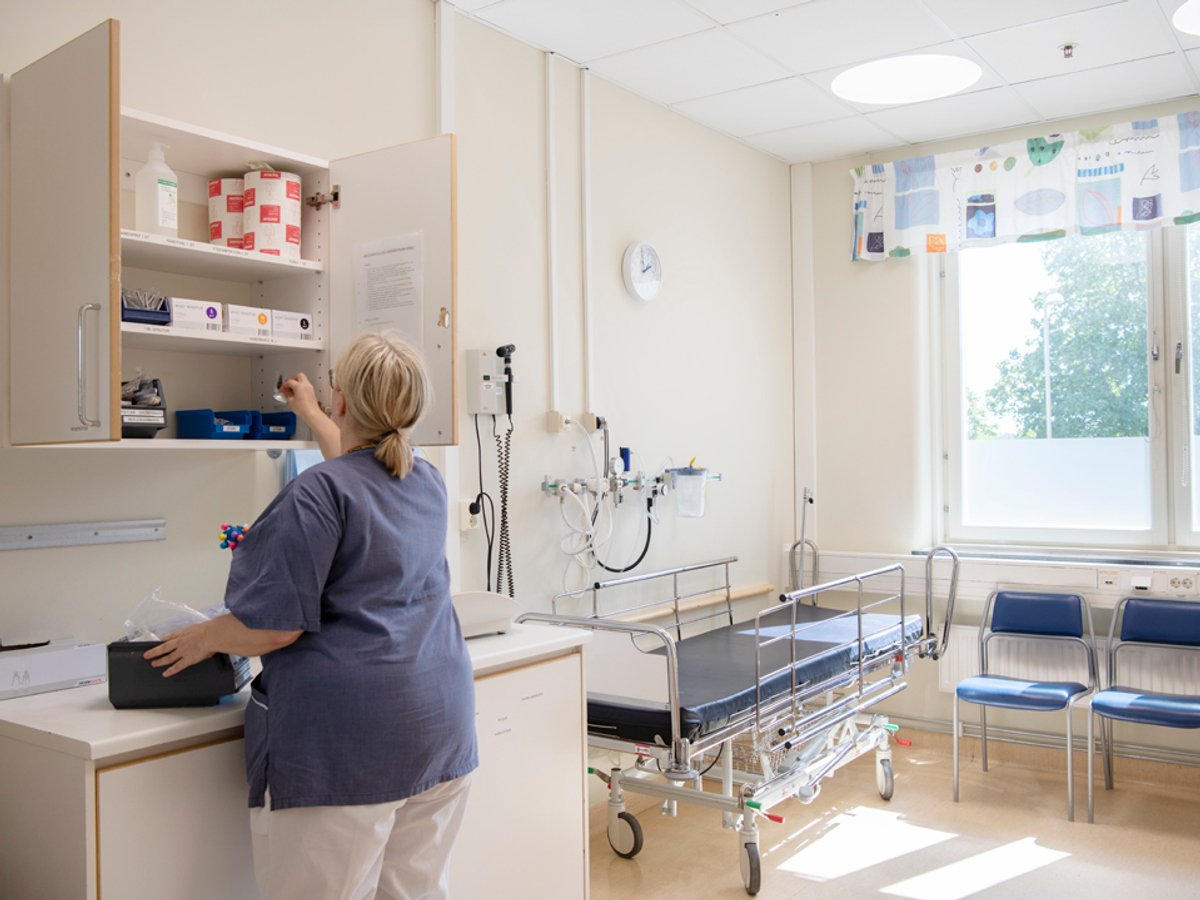 Bild på sjukhusrum med en brist och en kvinnlig personal som tar något från ett skåp