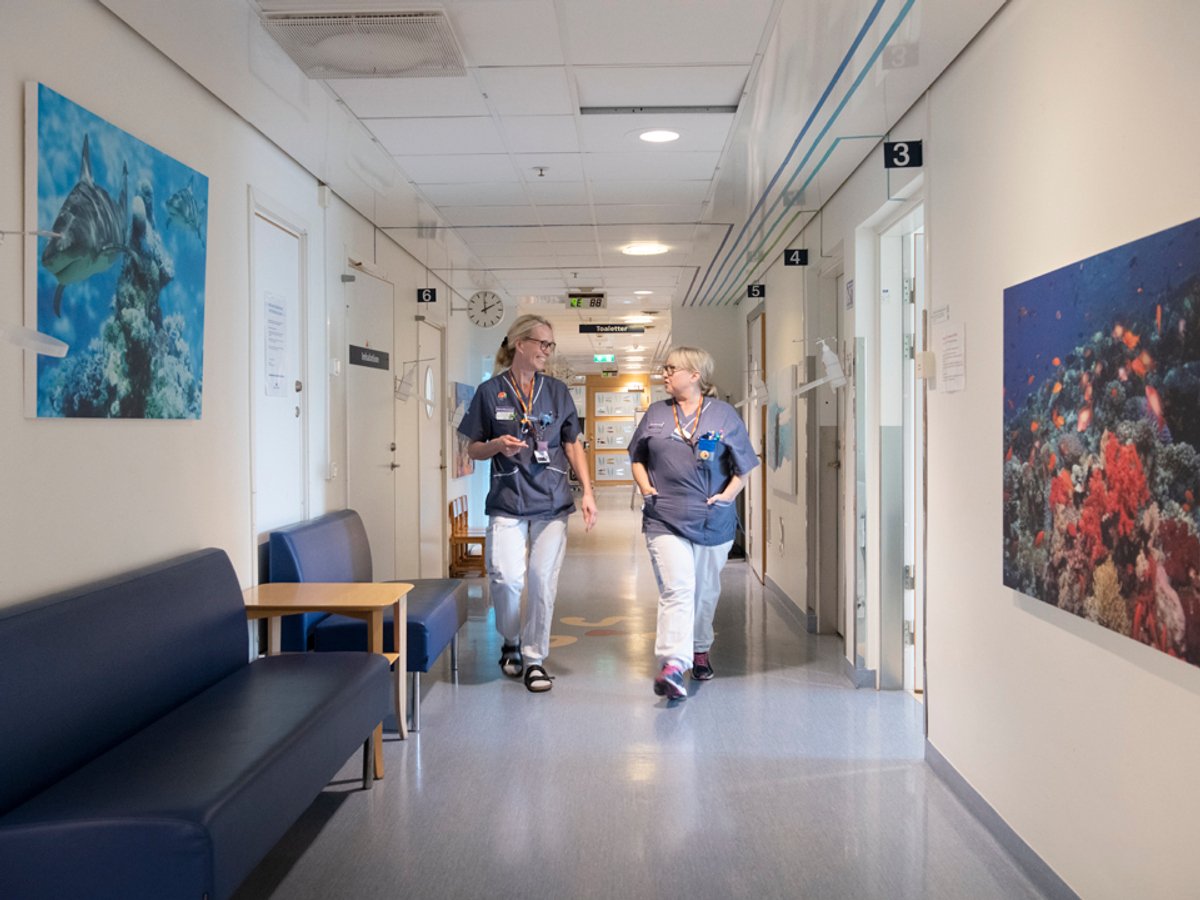 Två kvinnor i sjukhuskläder går i en korridor
