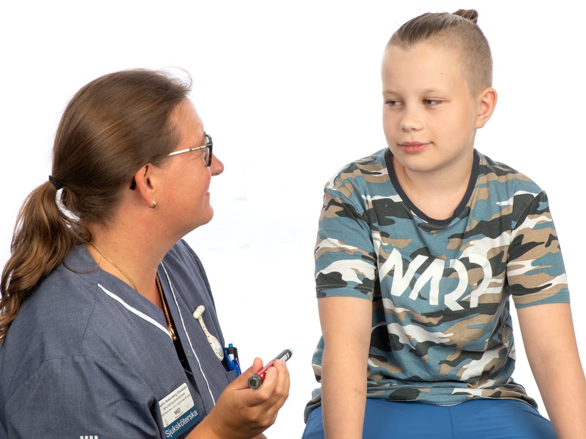 Kvinna i sjukhuskläder som håller i en insulinspruta sitter bredvid en ung pojke