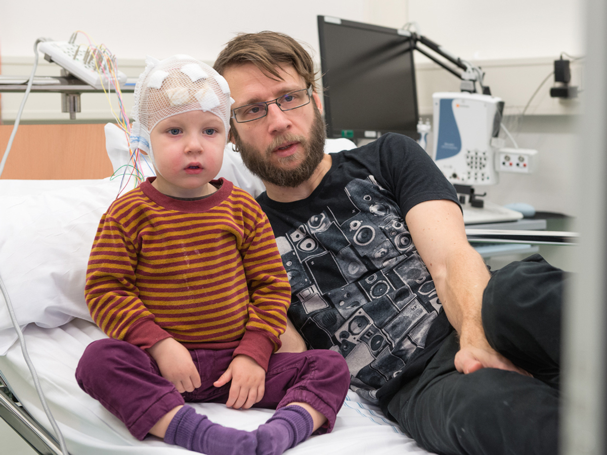 Bild på ett barn och en man sittandes på en sjukhussäng