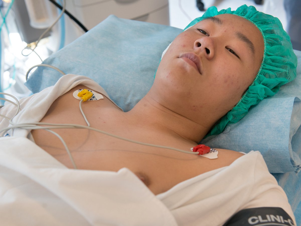 Ung man som ligger på ett operationsbord med sladdar på bröstet och en operationsmössa på sig