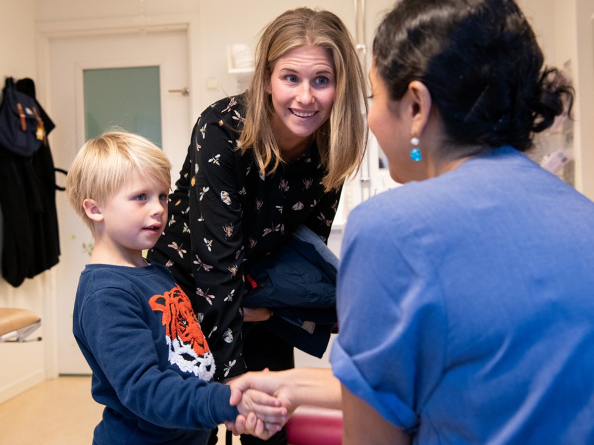Kvinna i sjukhuskläder som hälsar på en ung pojke som står bredvid en kvinna