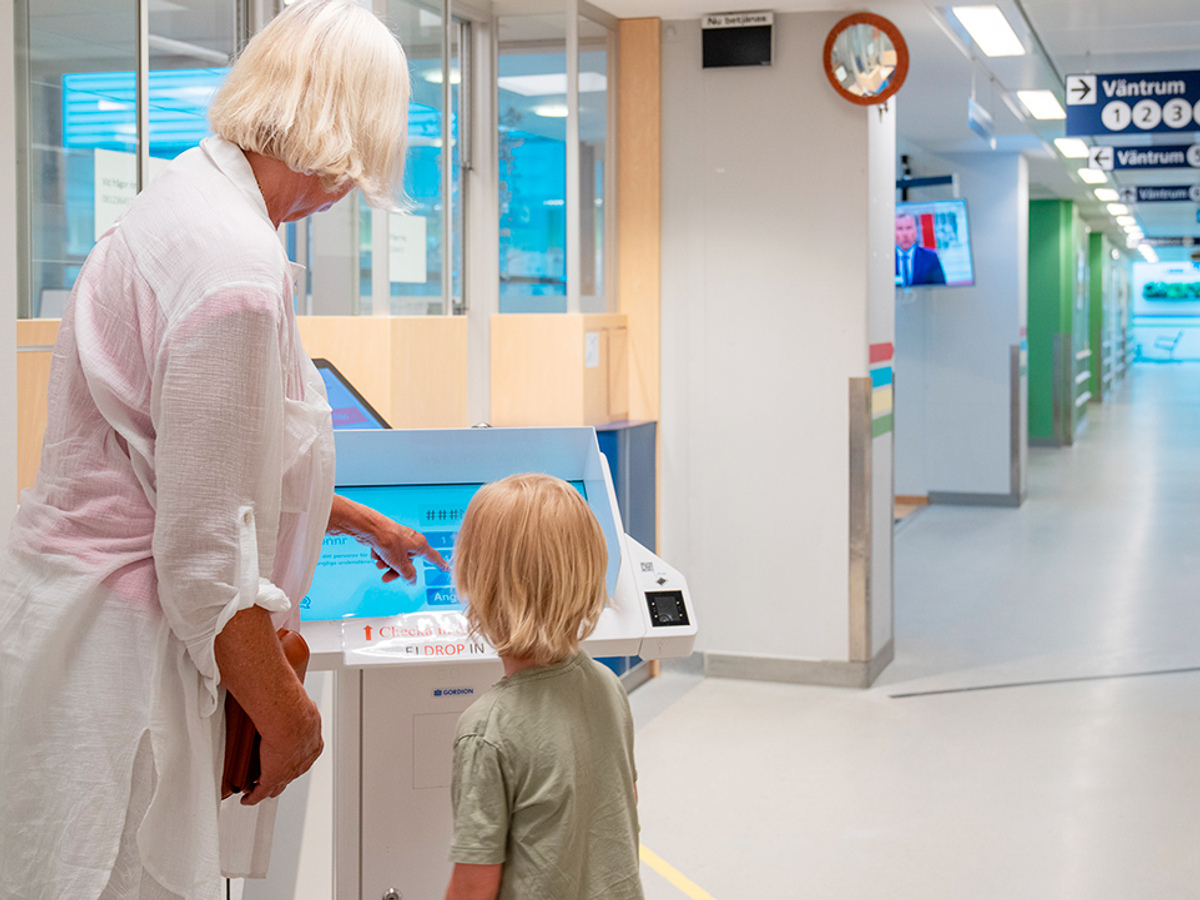 Två personer, en ung och en äldre, pekar på en skärm i en sjukhuskorridor