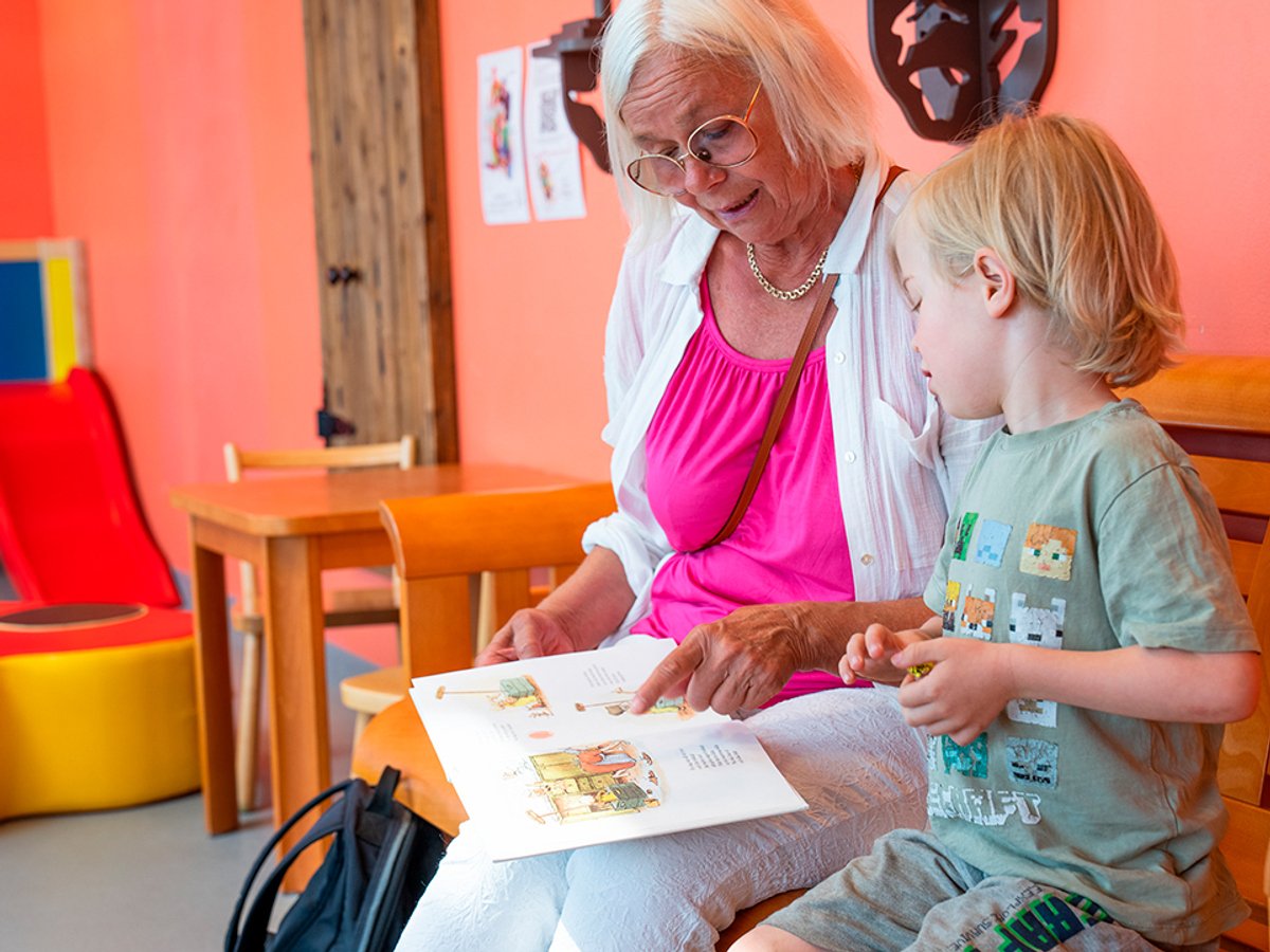 En äldre kvinna och en ung pojke som sitter i ett väntrum och läser en bok