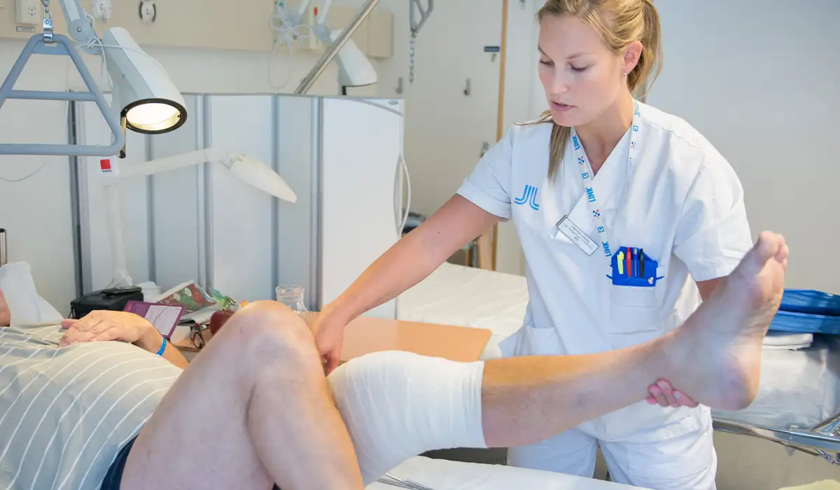 Bild på kvinna i sjukhuskläder som håller i ett ben med bandage på