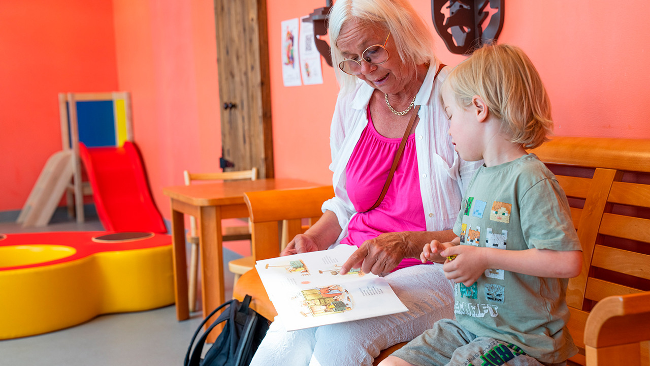 En äldre kvinna och en ung pojke som sitter i ett väntrum och läser en bok