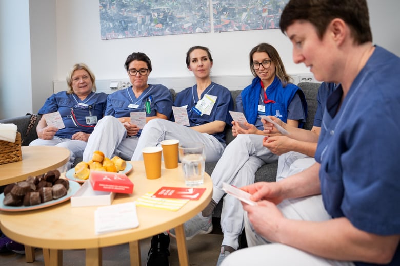 En grupp v&aring;rdpersonal i arbetskl&auml;der som sitter runt ett tr&auml;bord spelar ett spelkort fr&aring;n Empatigymmet.