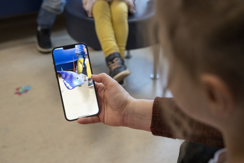 Ett barn som h&aring;ller en mobiltelefon i handen med en fisk p&aring; sk&auml;rmen.