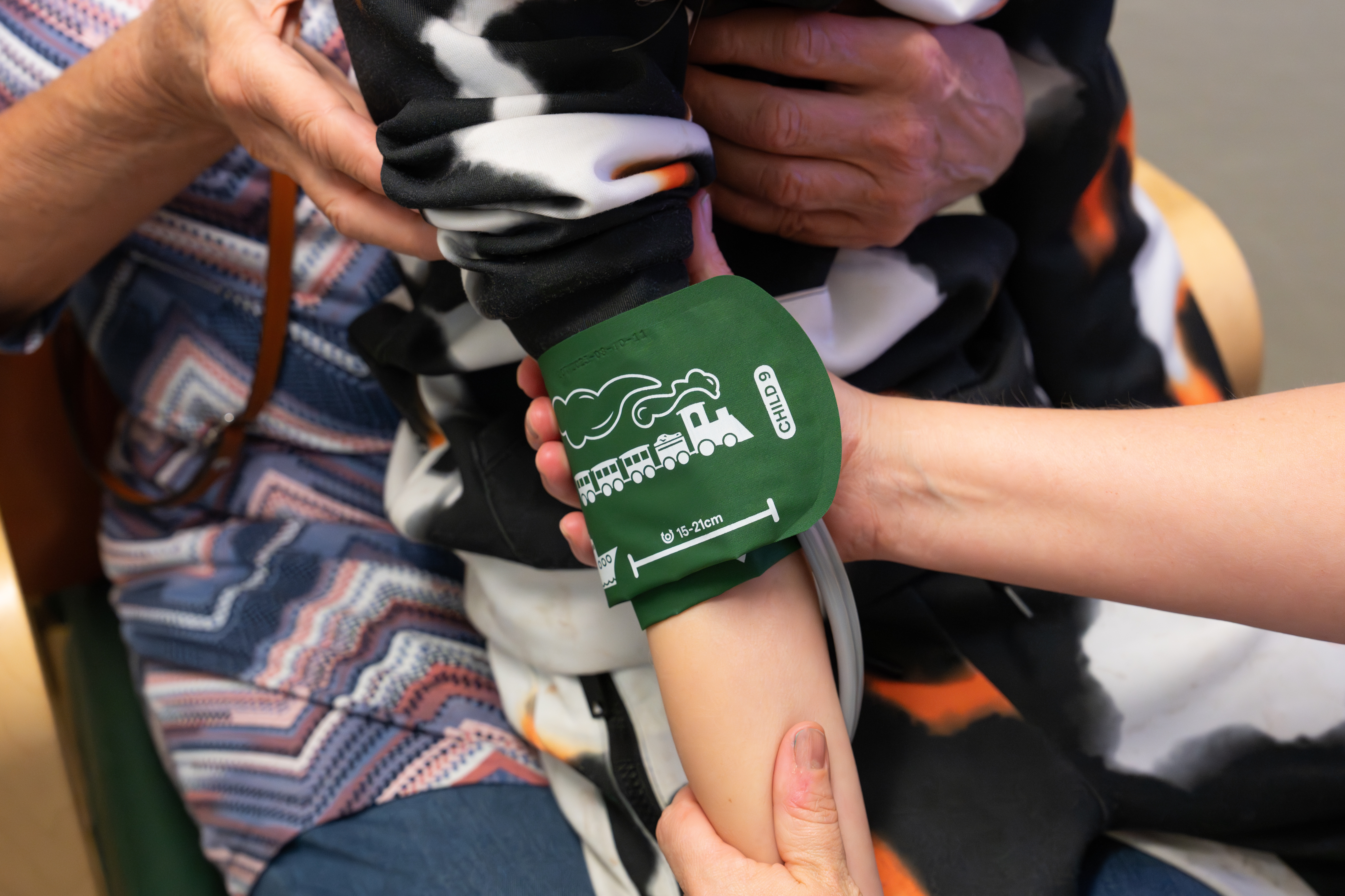 En person som h&aring;ller ett barns arm med ett gr&ouml;nt armband f&ouml;r att m&auml;ta blodtryck.