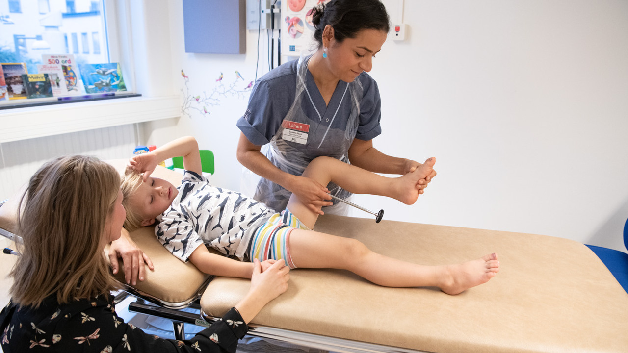 En kvinna h&aring;ller i en ung pojkes ben och en reflexhammare