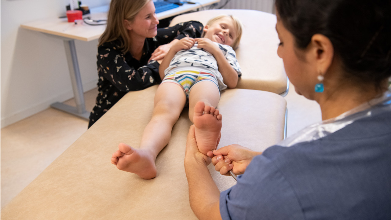 En kvinna i sjukhuskl&auml;der testar k&auml;nseln p&aring; en ung pojkes fotsula