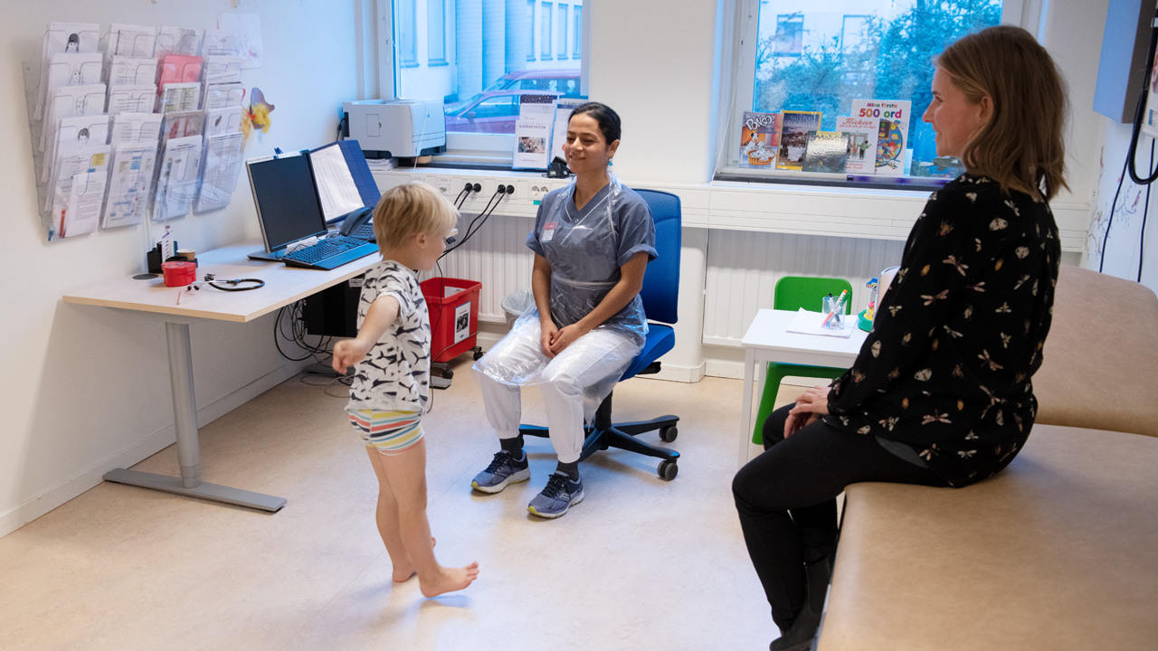 Tv&aring; kvinnor tittar p&aring; en ung pojke som balanserar p&aring; h&auml;larna i ett unders&ouml;kningsrum