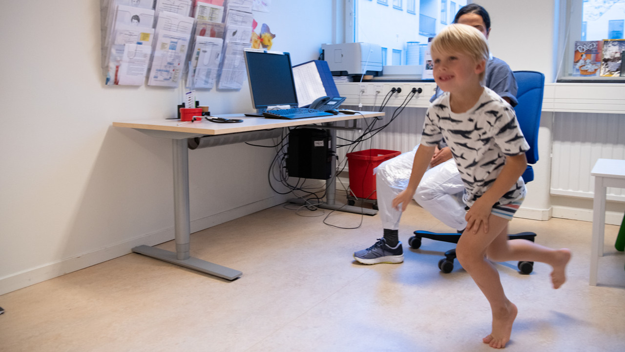 En ung pojke springer p&aring; t&aring;rna i ett unders&ouml;kningsrum framf&ouml;r en kvinna i sjukhuskl&auml;der