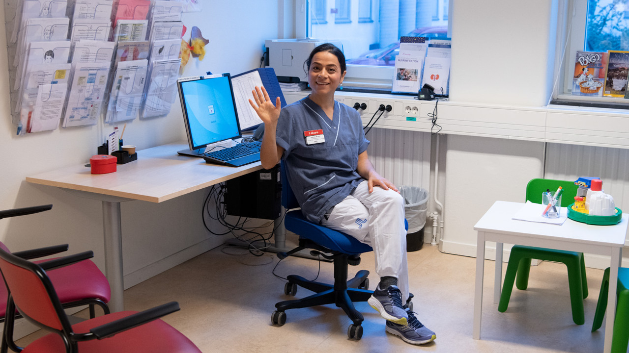 En kvinna i sjukhuskl&auml;der sitter p&aring; en stol och vinkar