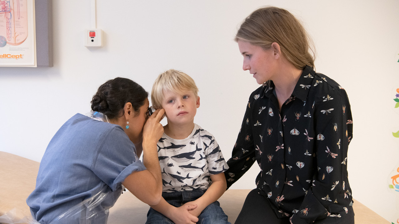 En kvinna i sjukhuskl&auml;der som unders&ouml;ker en ung pojkes &ouml;ra