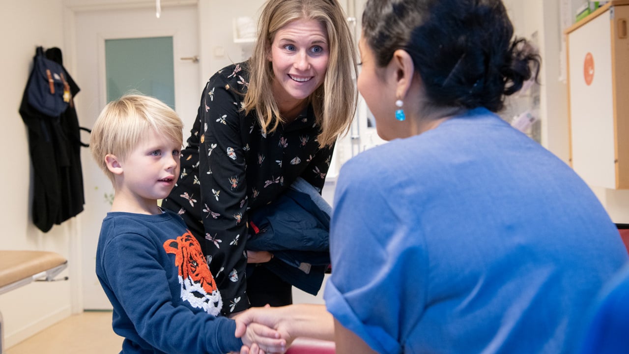 En kvinna i sjukhuskl&auml;der som h&auml;lsar p&aring; en ung pojke