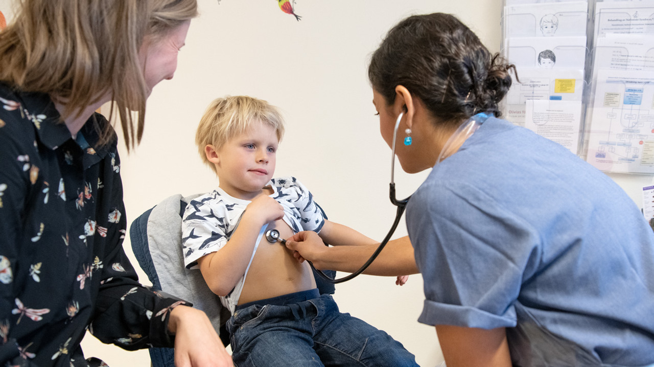 Ett barn som blir unders&ouml;kt med stetoskop p&aring; magen av en kvinna i sjukhuskl&auml;der