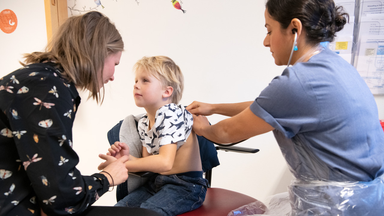 Ett barn som blir unders&ouml;kt med stetoskop p&aring; ryggen av en kvinna i sjukhuskl&auml;der