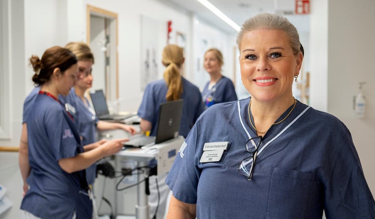 Bild på en kvinna som är vårdenhetschef med 5 kvinnor i sjukhuskläder i bakgrunden 