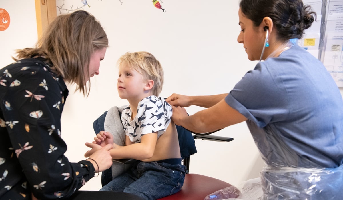 Ett barn som blir undersökt med stetoskop på ryggen av en kvinna i sjukhuskläder