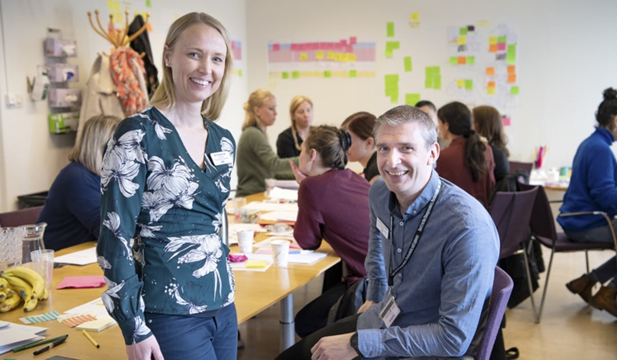 En man och en kvinna sitter vid ett bord framför en grupp människor.