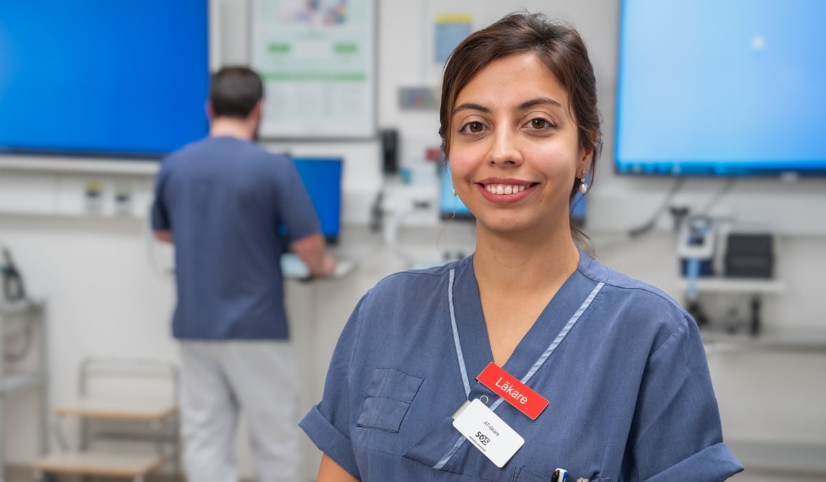 Bild på en AT-läkare som står i ett sjukhusrum med sjukhuskläder