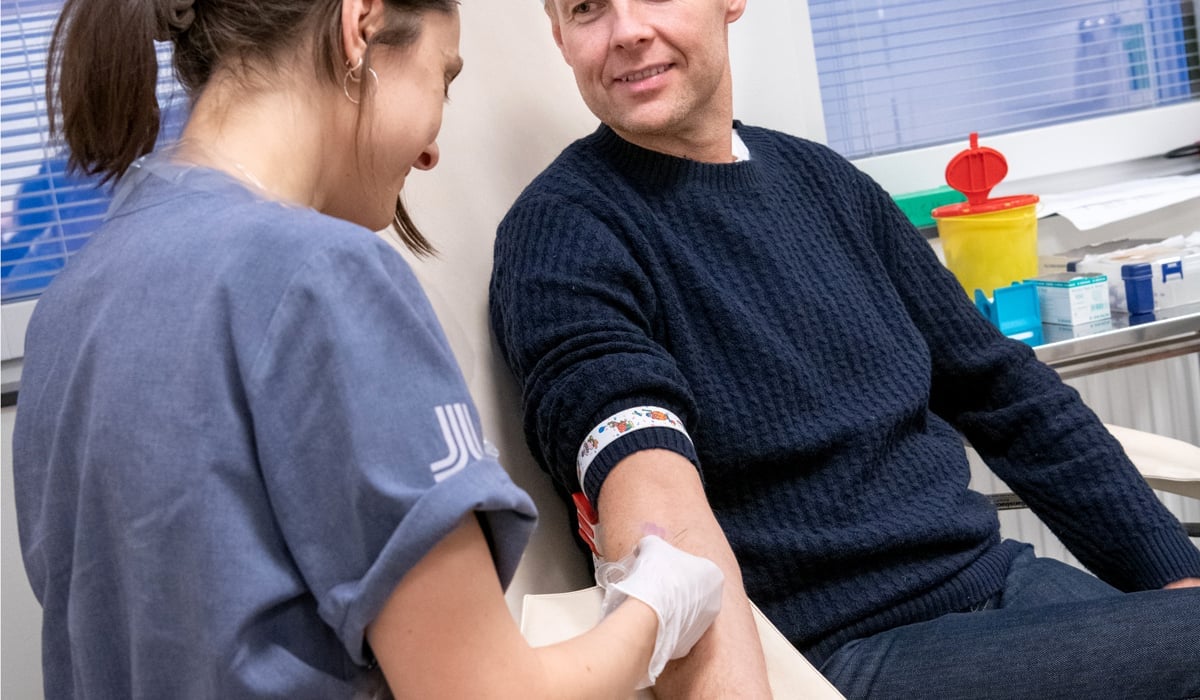 Bild på en kvinna i sjukhuskläder som tar ett blodprov på en man som sitter i en sjukhusstol
