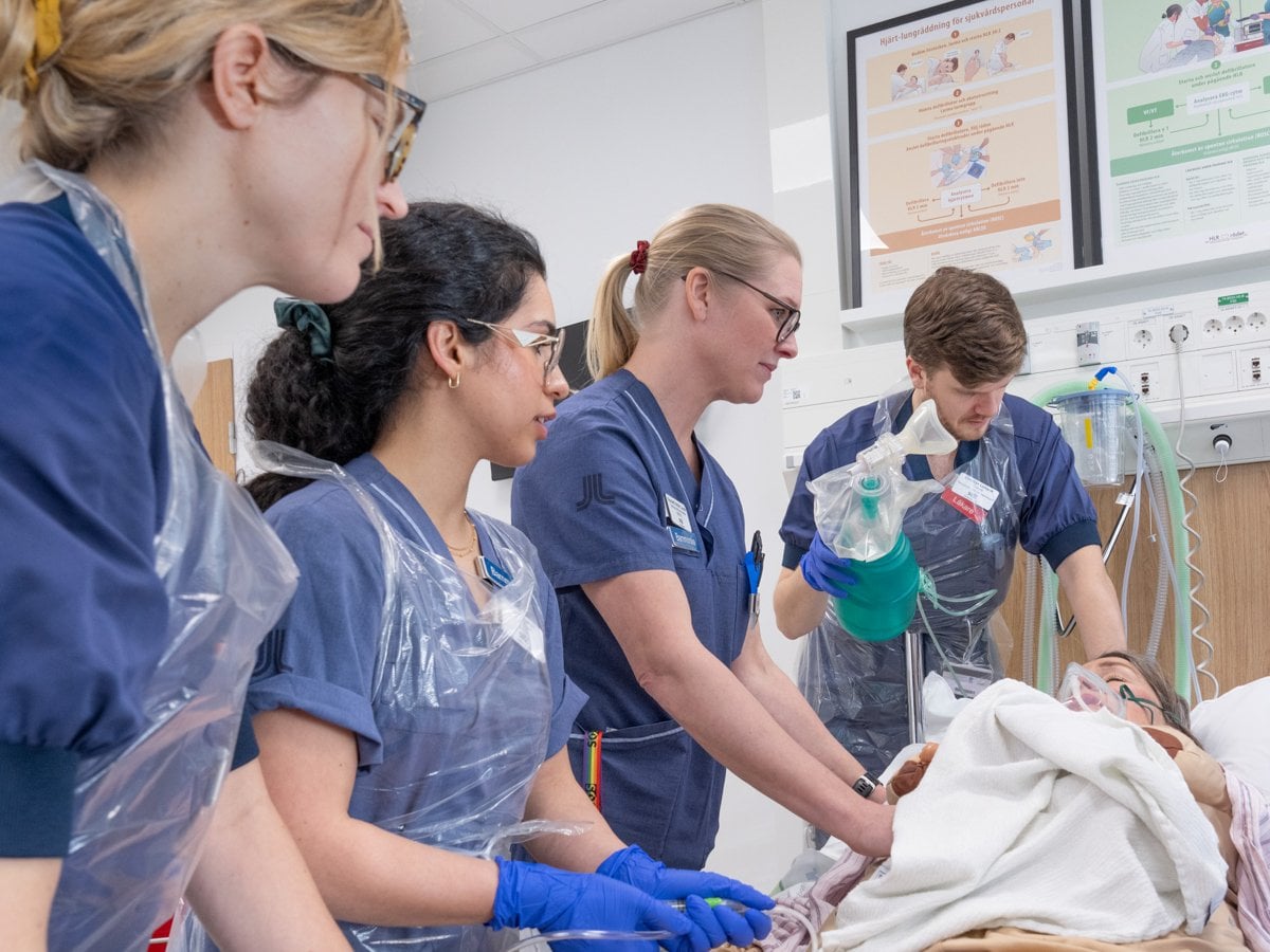 Bild på 5 personer i sjukhuskläder, en man 4 kvinnor, som utför en övning på en person som agerar patient.