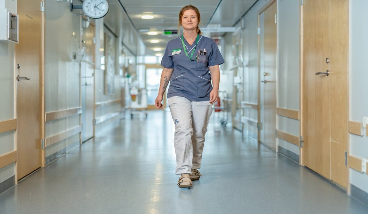 kvinnlig undersköterska går genom sjukhuskorridor