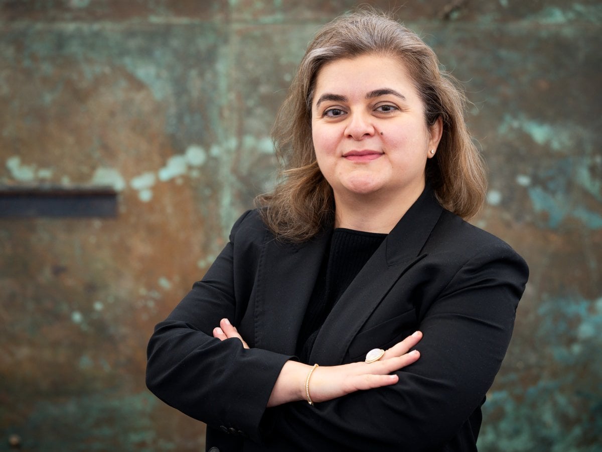 Porträtt Elham Hedayati i svart kavaj med armarna i kors framför konstverk i brons.