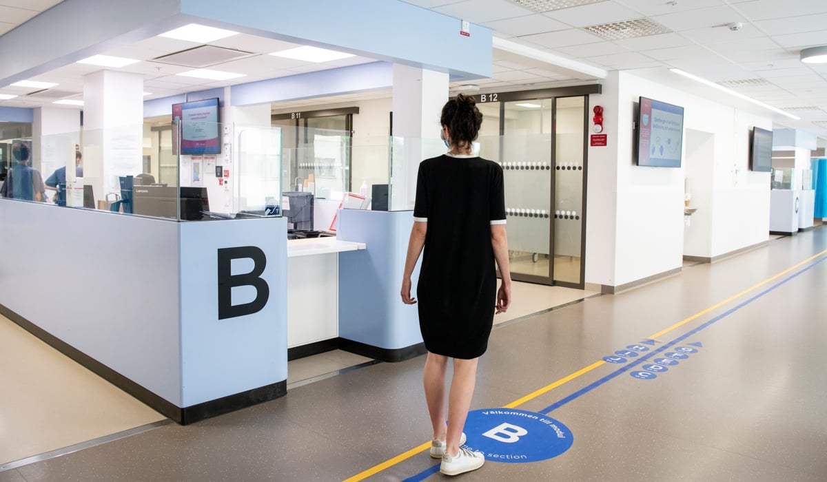 Kvinna med privata kläder som står vid en reception i en sjukhuskorridor