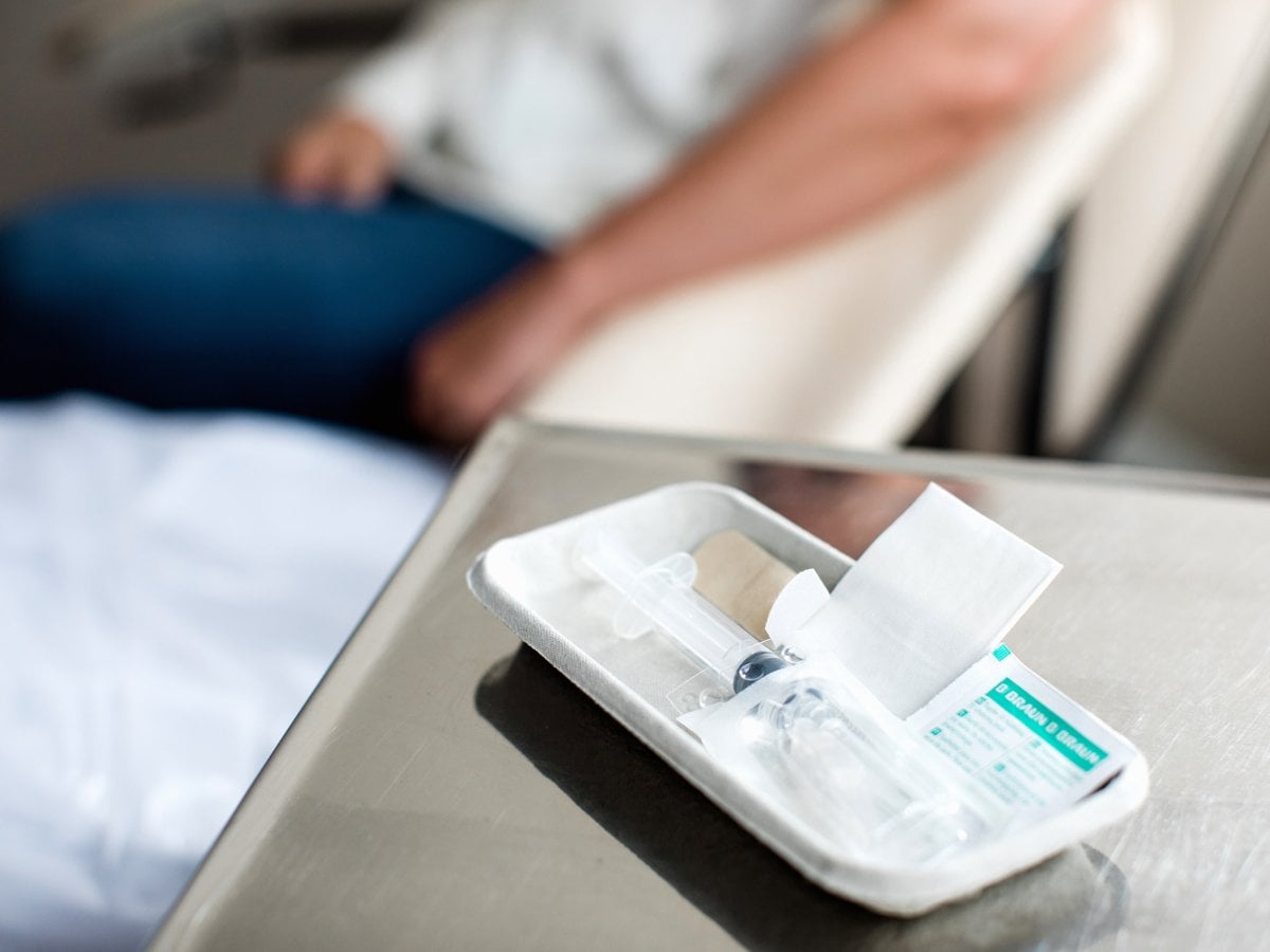 Bild på en kartongbehållare med spruta, tvättlapp, plåster och annat material. En arm syns i bakgrunden