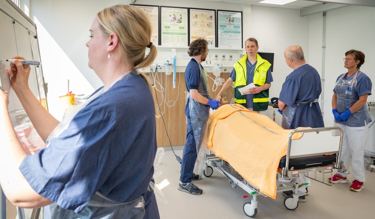 Fem personer med sjukhuskläder som står i ett övningsrum