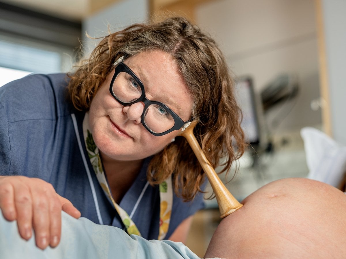 Barnmorska lyssnar på gravid mage med trätratt