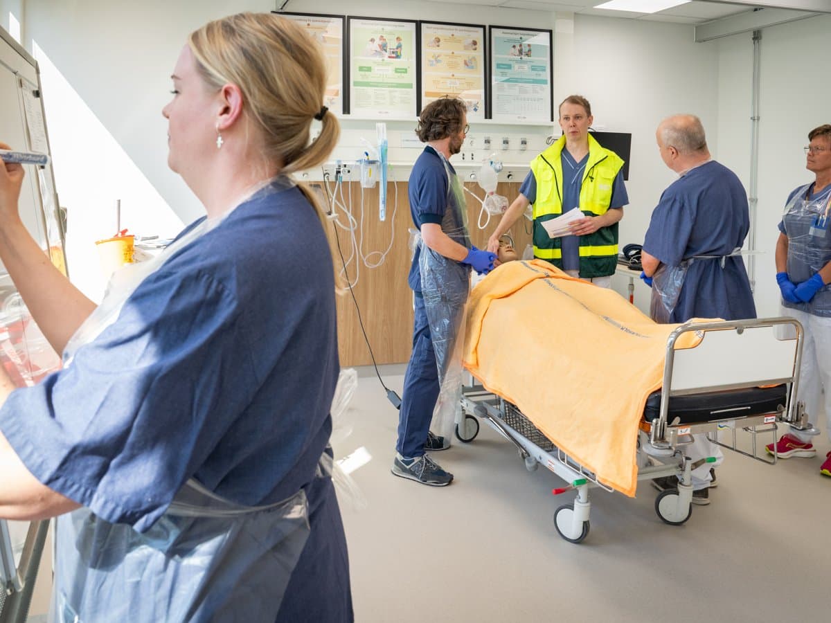 Fem personer med sjukhuskläder som står i ett övningsrum