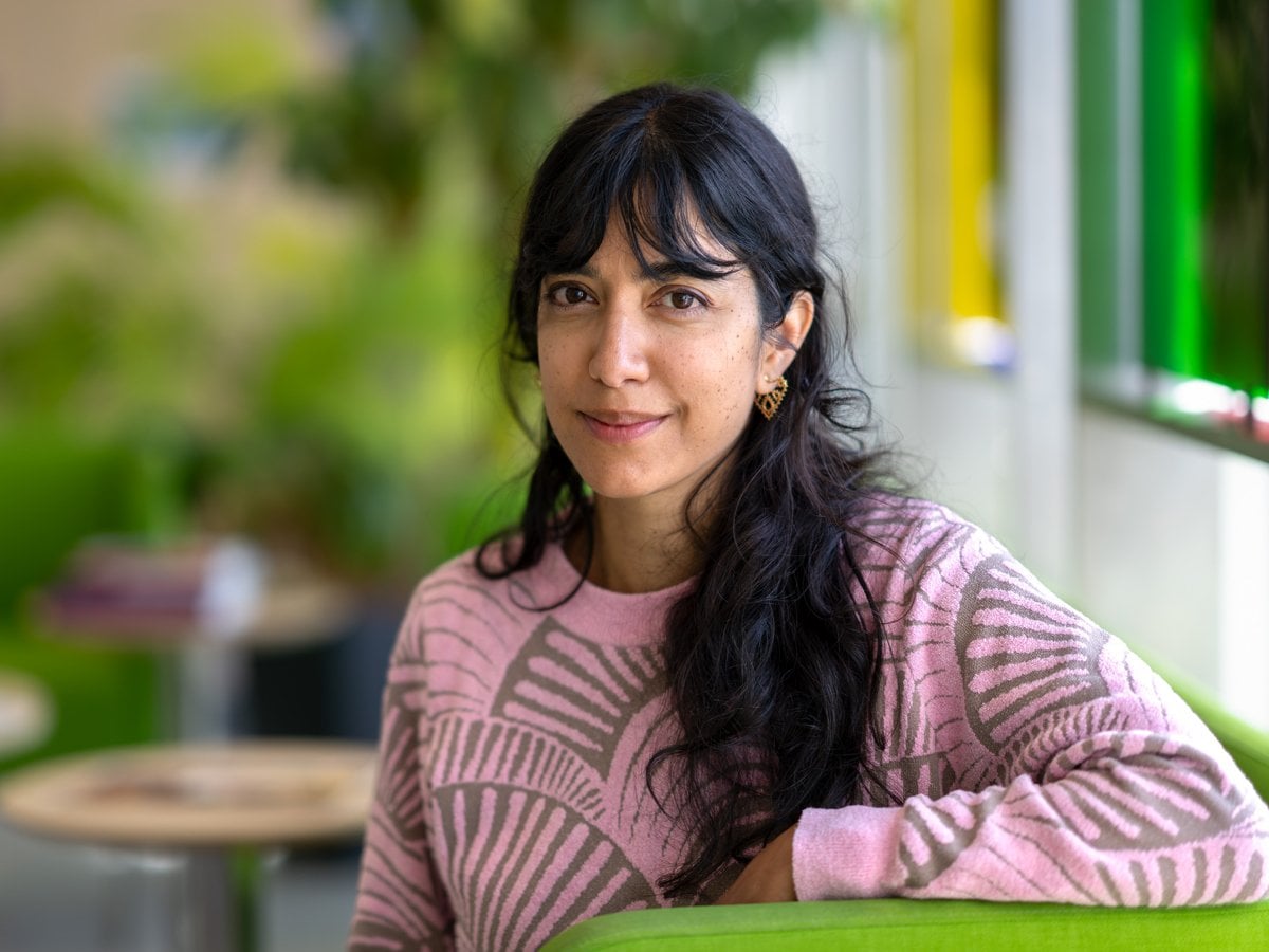 Shabane Barot i rosa tröja. långt mörk hår, lutar arm mot grönt ryggstöd.