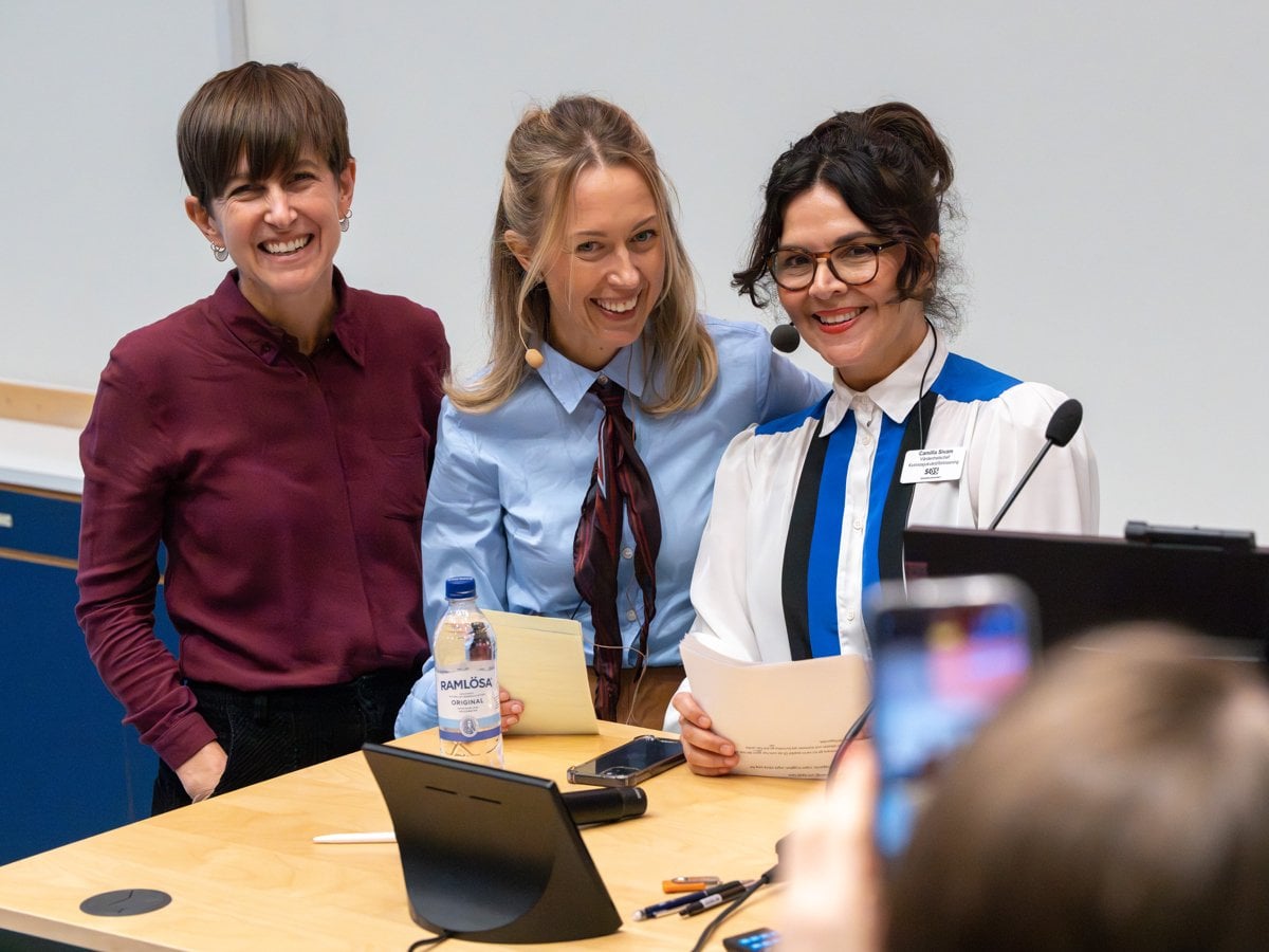 tre skrattande kvinnor vid talarbänk