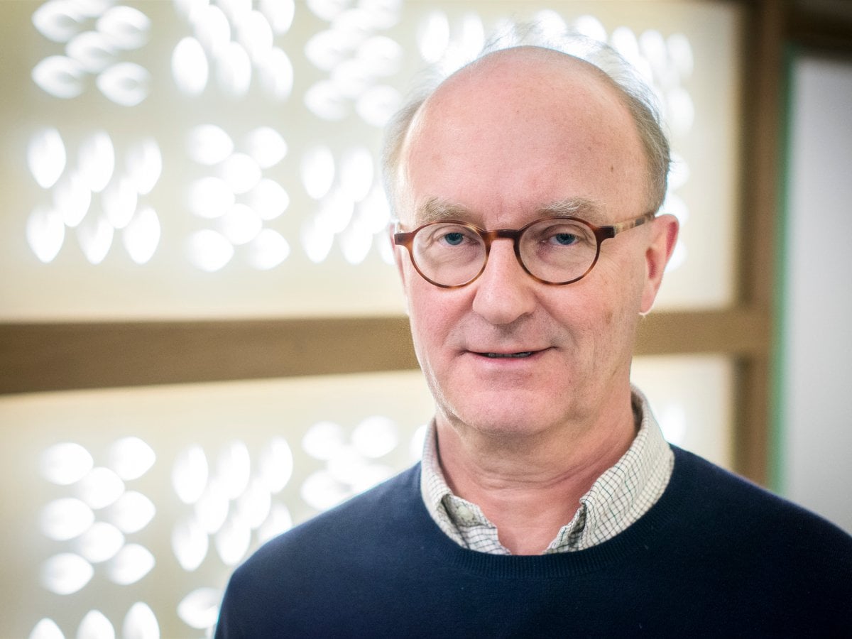 En man med glasögon står framför en vägg.