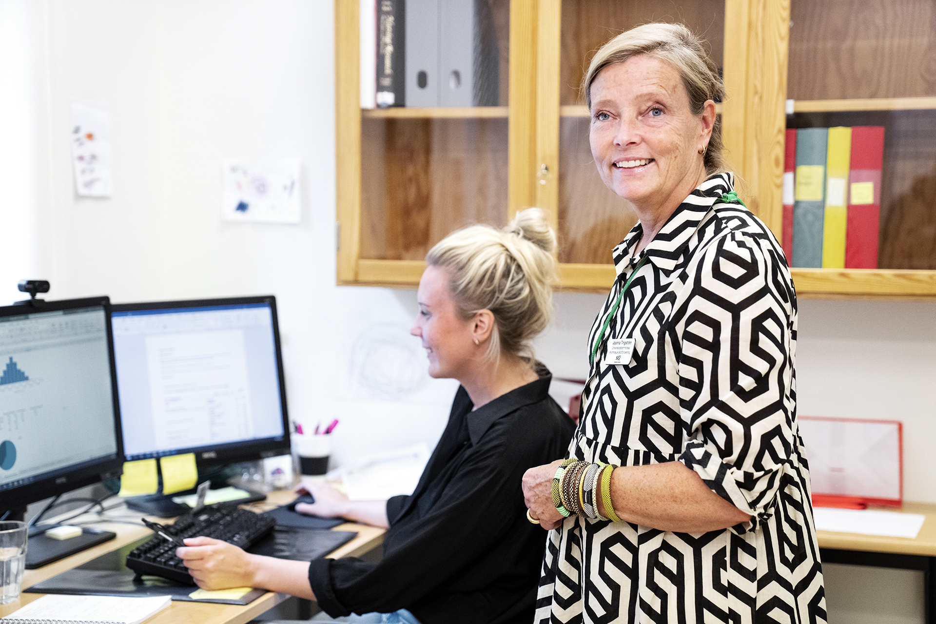 Joanna Tingström står i ett kontorsrum. I bakgrunden en yngre kvinna som sitter framför en datorskärm.
