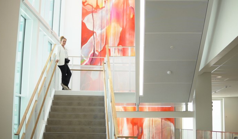 kvinna står i trappa framför stort konstverk i rött-orange
